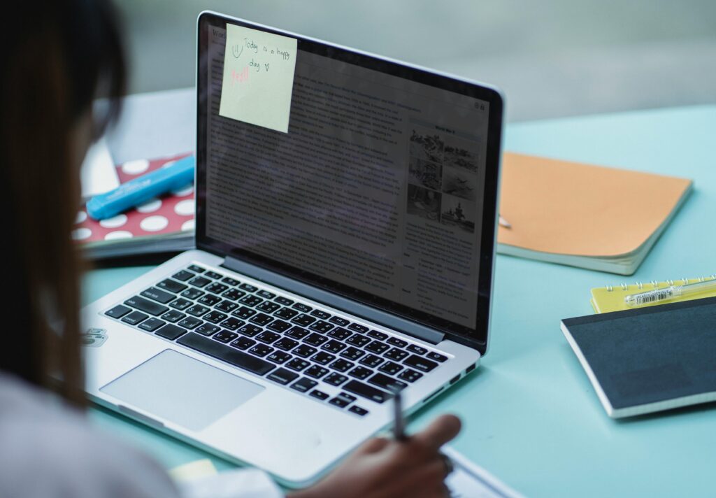 pexels photo 5537527 5537527 Crop multiracial friends watching netbook with text on screen and sticker while writing on paper