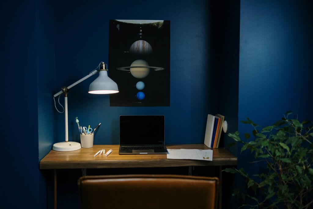 pexels photo 7014764 7014764 A modern home office with blue walls, desk lamp, and open laptop, creating a focused workspace.